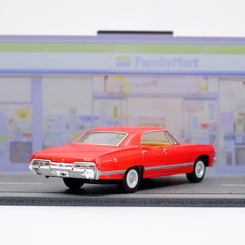 A red 1967 Chevrolet Impala diecast model car in a pull-back action pose on a gray surface.
