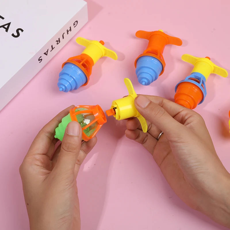 A hand holds a glow-in-the-dark spinning top in yellow and orange colors on a pink background.