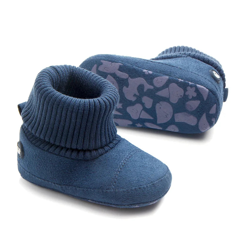 A navy blue baby winter snow boot with a fuzzy ball accent pattern lying next to the boot.