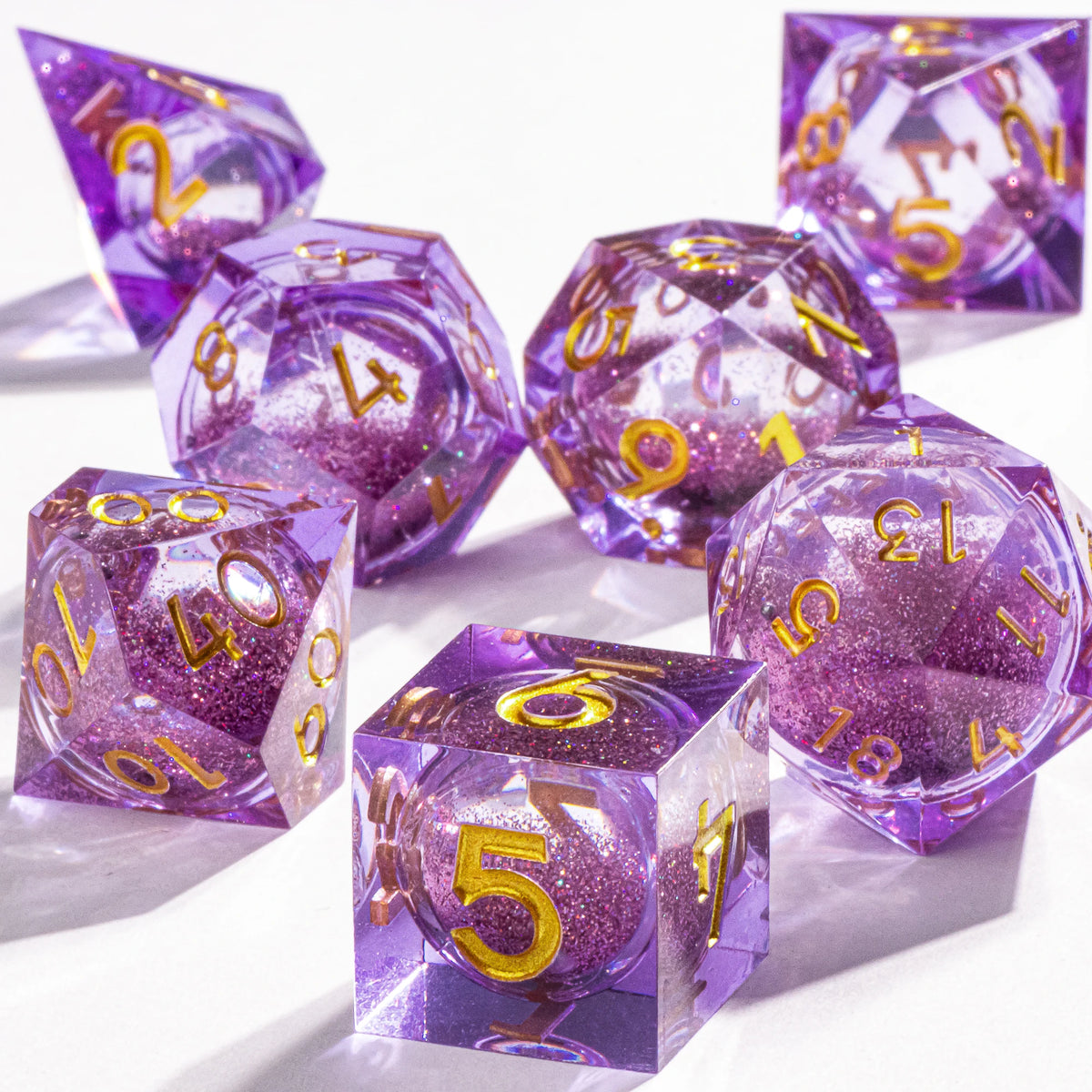A collection of purple polyhedral dice with a galaxy finish scattered on a white surface.
