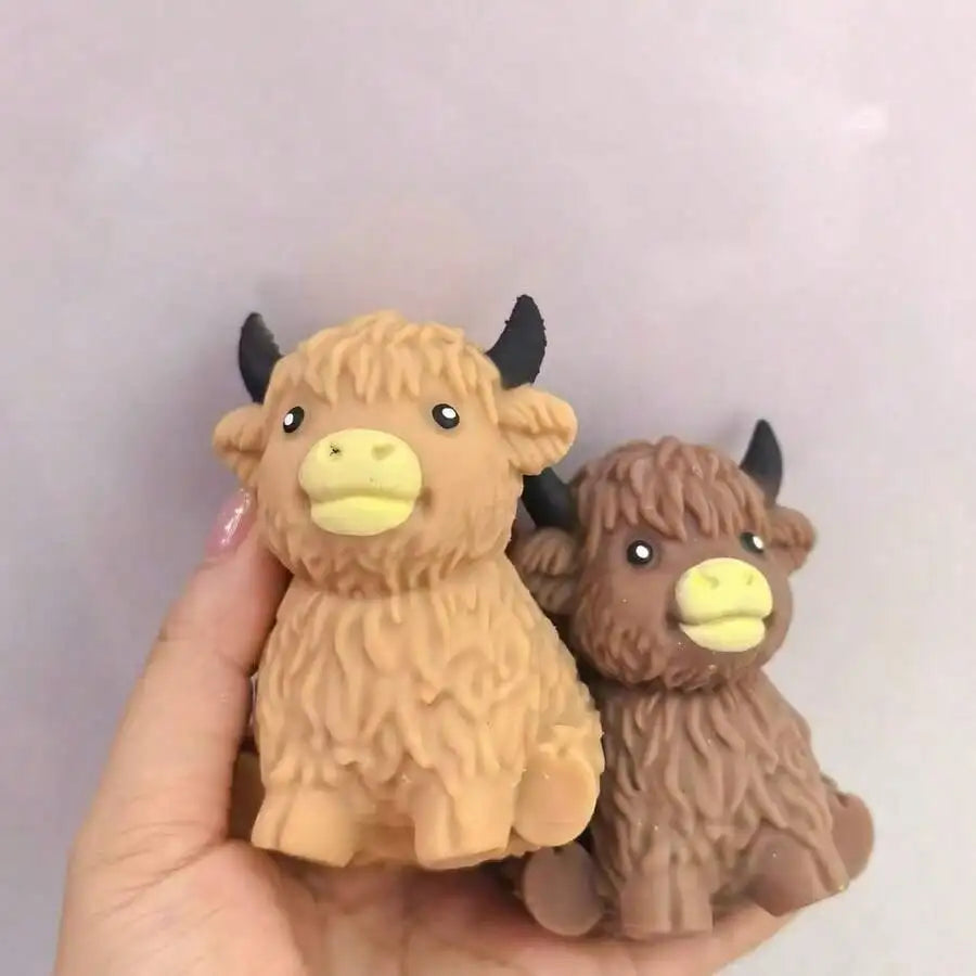 A hand holds a brown Scottish Highland cow stress relief squishy toy.