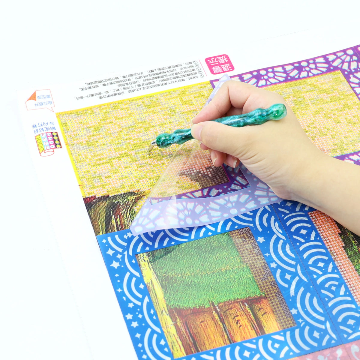 A hand is using a tool to release a green bead from a sheet of reusable non-stick release paper for diamond painting.