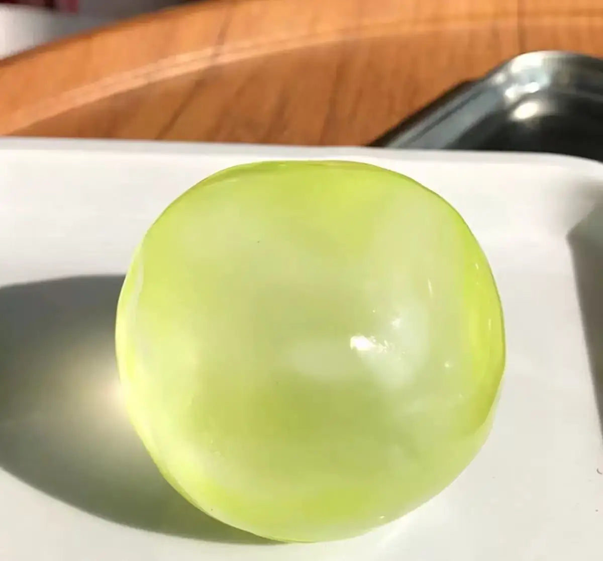 A translucent lime green squishy stress ball resting on a white plate.