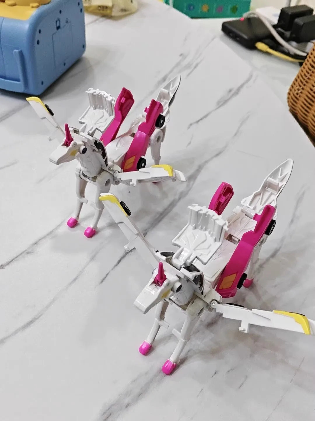 A white and pink transforming dinosaur car toy with a horse-like body and wings on a marble surface.