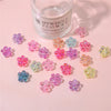 A collection of colorful acrylic flower beads in various shades of pink, purple, and green are displayed next to a glass jar 