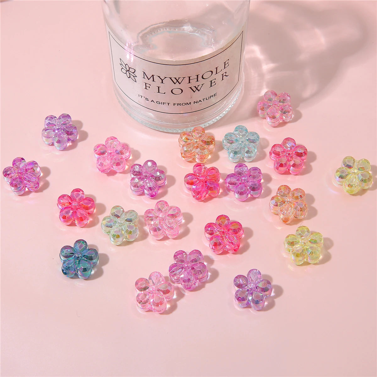 A collection of colorful acrylic flower beads in various shades of pink, purple, and green are displayed next to a glass jar 