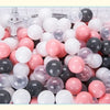 A large assortment of colorful play balls in various shades of pink, white, and black are displayed in a white basket.