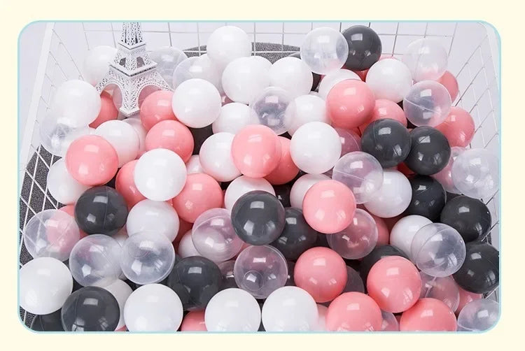 A large assortment of colorful play balls in various shades of pink, white, and black are displayed in a white basket.