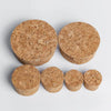 A set of four natural wood tapered bottle and test tube stoppers in various shades of light brown.