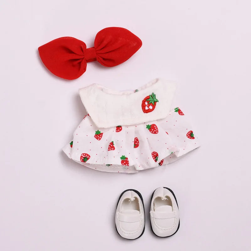 A red bow and a white strawberry print outfit with matching princess shoes for a doll.