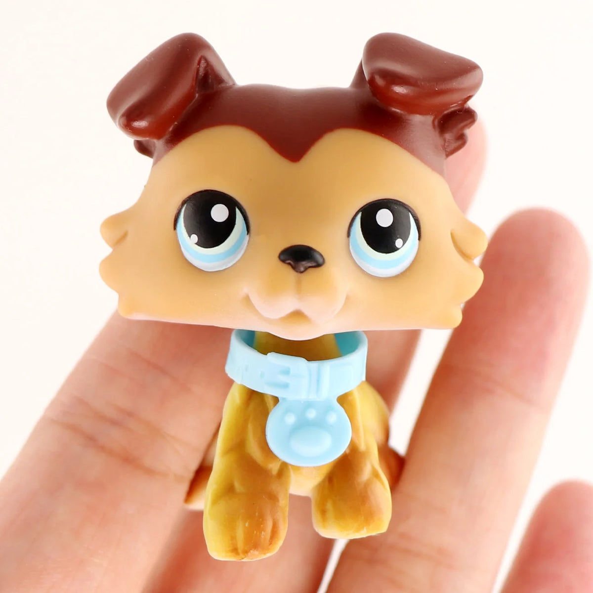A small, brown and tan miniature pet animal figure with large blue eyes and a light blue collar.