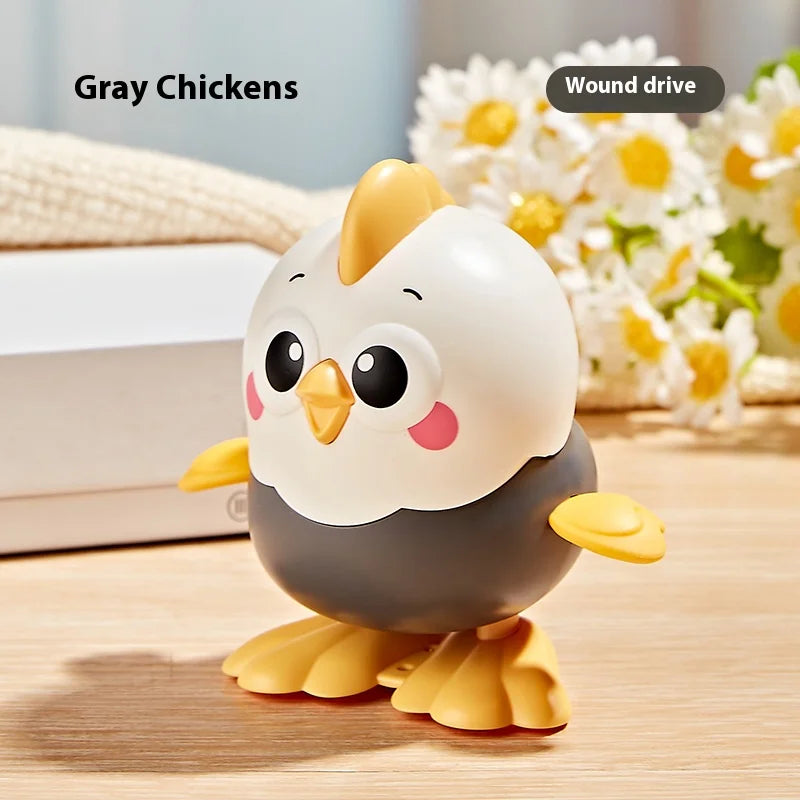 A gray chicken wind-up toy with yellow accents sitting on a wooden surface next to white and yellow flowers.