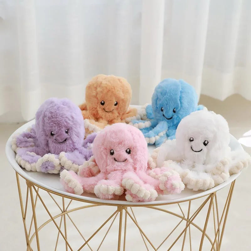 A collection of soft, pastel-colored octopus plush toys in purple, orange, blue, pink, and white resting on a gold wire stand