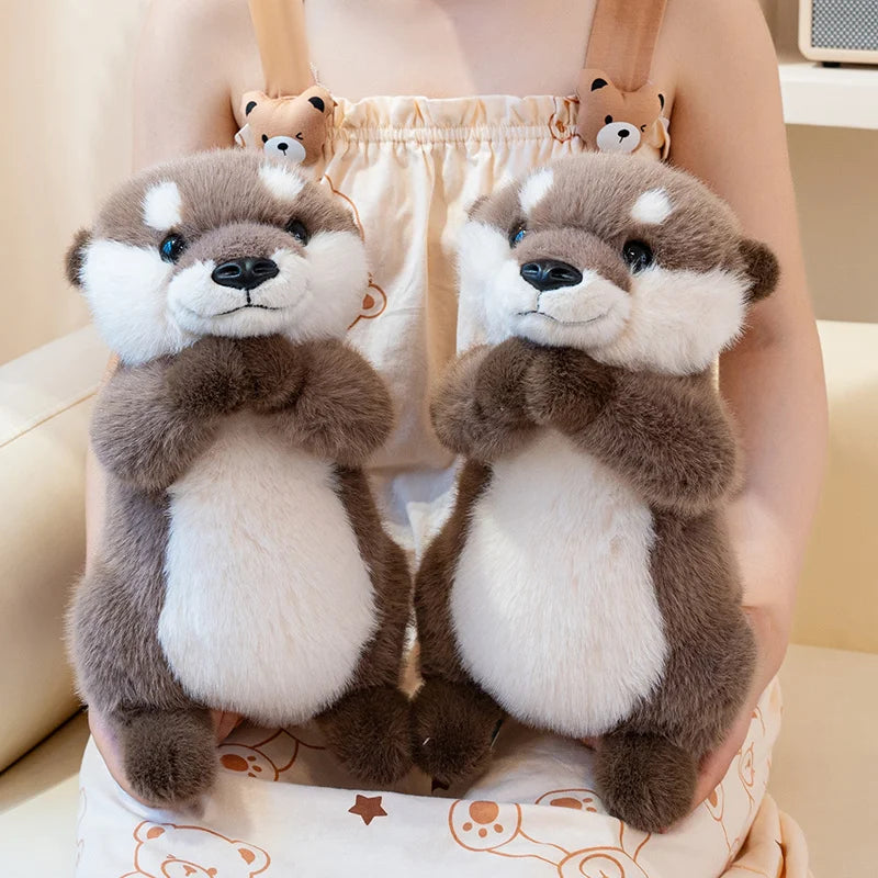 A pair of soft, gray and white magnetic otter plush toys are shown being held in a person's arms.