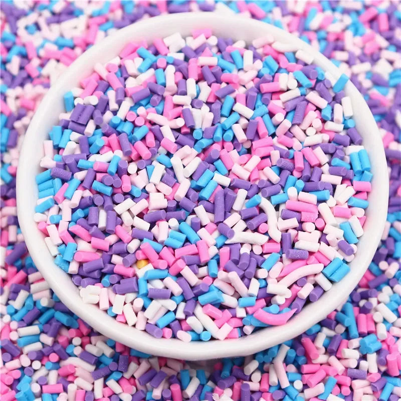 A white bowl filled with colorful polymer clay slice sprinkles in various shades of pink, blue, and purple scattered on a sur