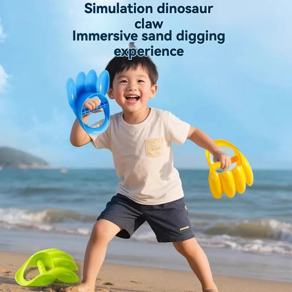 A smiling boy is playing with a blue dinosaur claw toy while digging in the sand near the ocean.