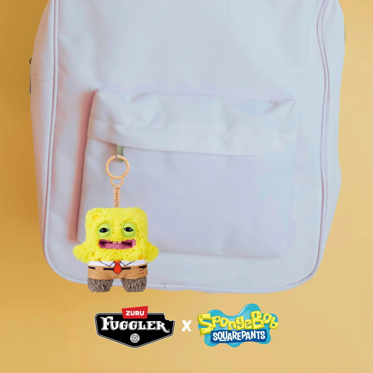 A yellow plush monster keychain with a rabbit design is displayed inside a pink backpack.