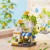 A mini building set featuring a woodland cabin and windmill structure with yellow flowers and green foliage.