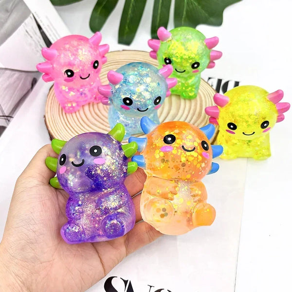 A collection of colorful axolotl squishy sensory fidget toys in pink, blue, green, and yellow are displayed on a wooden surfa