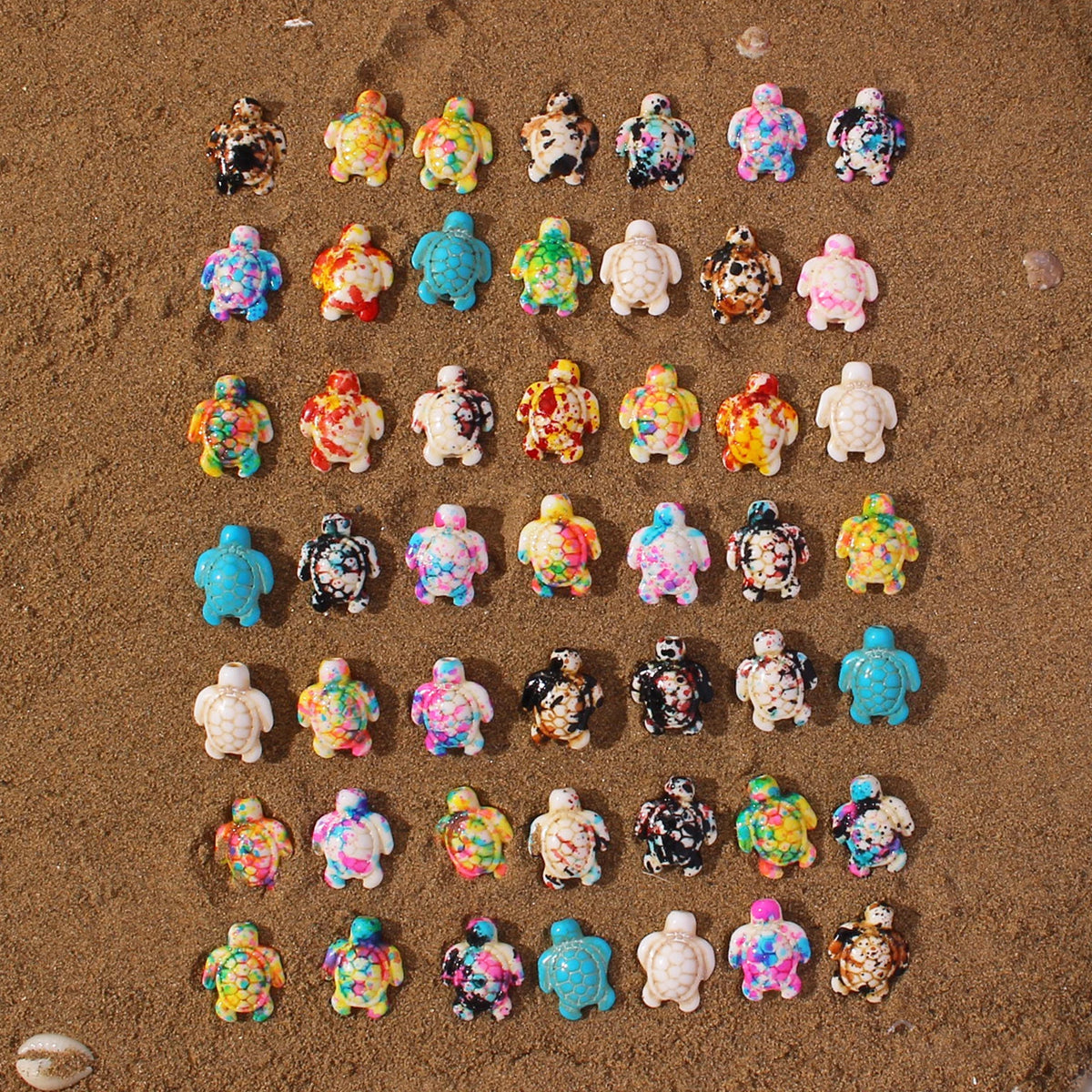 A collection of multicolor ocean turtle beads scattered on sand for jewelry making