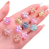 A hand holds several small, translucent acrylic flower beads in various shades of pink and purple.