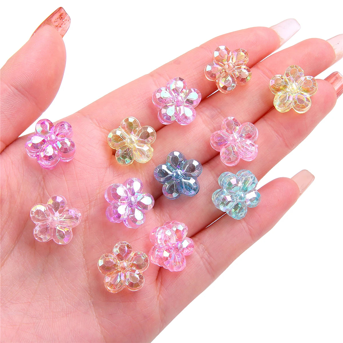 A hand holds several small, translucent acrylic flower beads in various shades of pink and purple.
