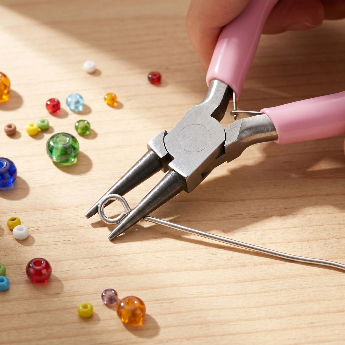 A hand uses pink pliers to grip a wire, demonstrating a jewelry making tool kit.