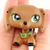 A small, brown miniature pet animal figure with large green eyes and a green collar is held in a person's hand.