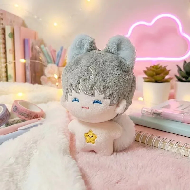 A light blue anime plush charm with fluffy ears and a smiling face resting on pink faux fur.