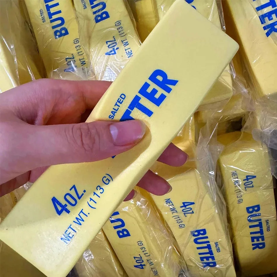 A hand holds a yellow butter squishy stress relief toy packaged in clear plastic.