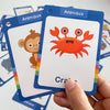 A hand holds a blue flash card titled Animaux featuring an orange crab illustration.