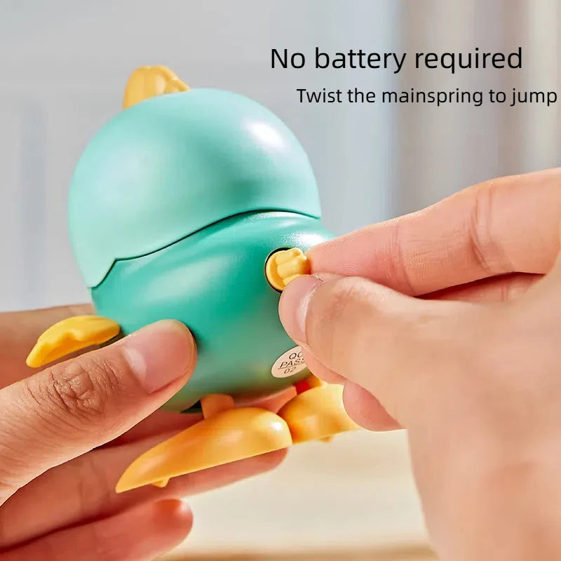 A hand twists a yellow pull chain on a light blue wind-up chick toy to make it jump.