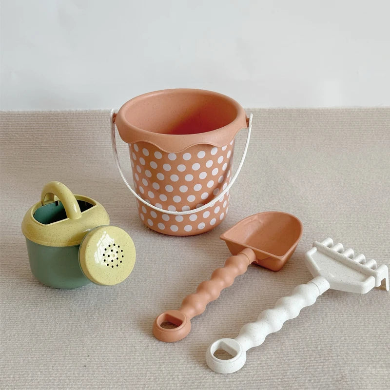 A set of orange and white plastic sand and water play items including a bucket, shovel, and a pull-along bulldozer trolley.