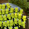 A collection of handmade crochet frog keychains in various shades of lime green and yellow clustered on a dark surface.