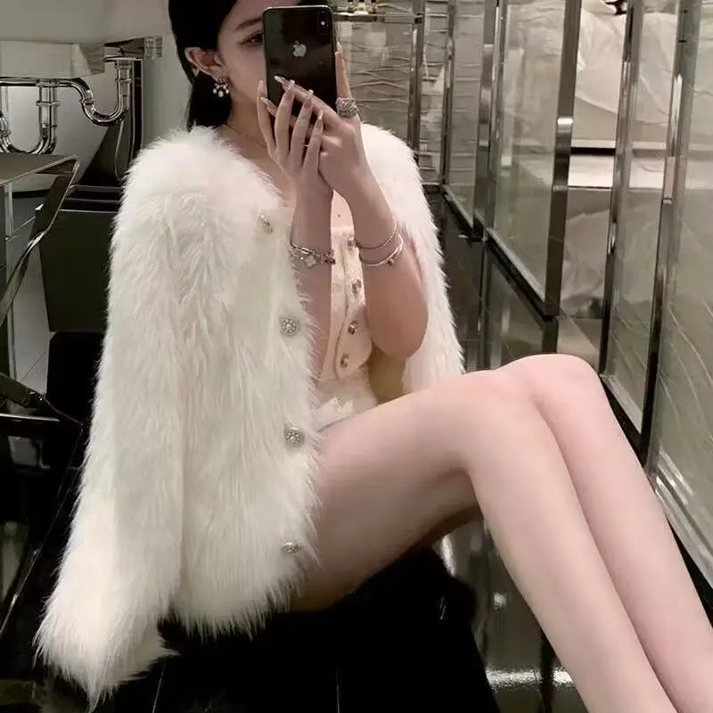 A woman models a white faux fur cardigan sweater while sitting in a modern glass-walled room.