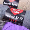 A close-up of a package of Super Soft Yarn with a red heart label and purple yarn visible in the foreground.