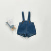 A pair of dark blue denim overalls or romper with straps and pockets lying on a light gray background.