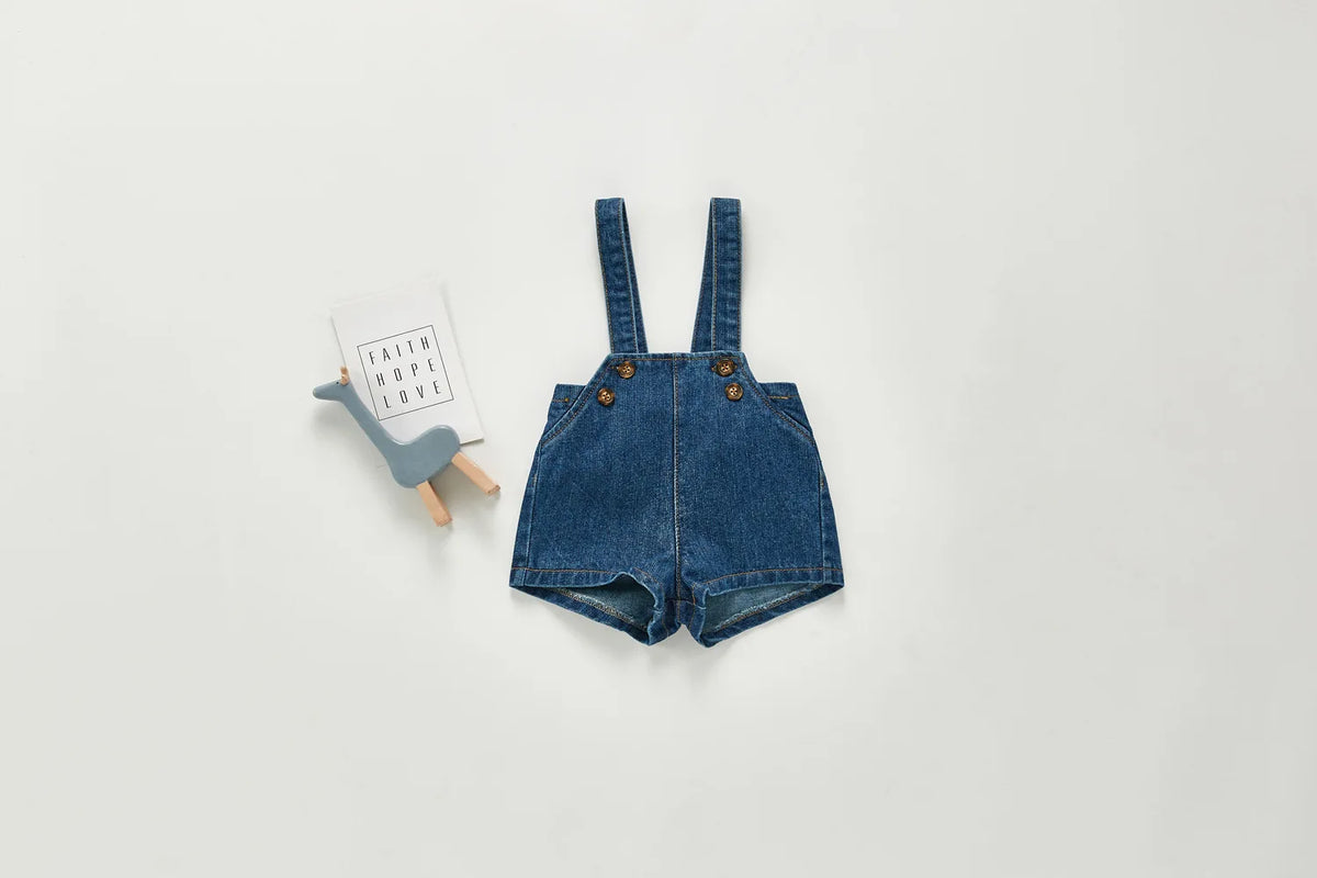 A pair of dark blue denim overalls or romper with straps and pockets lying on a light gray background.