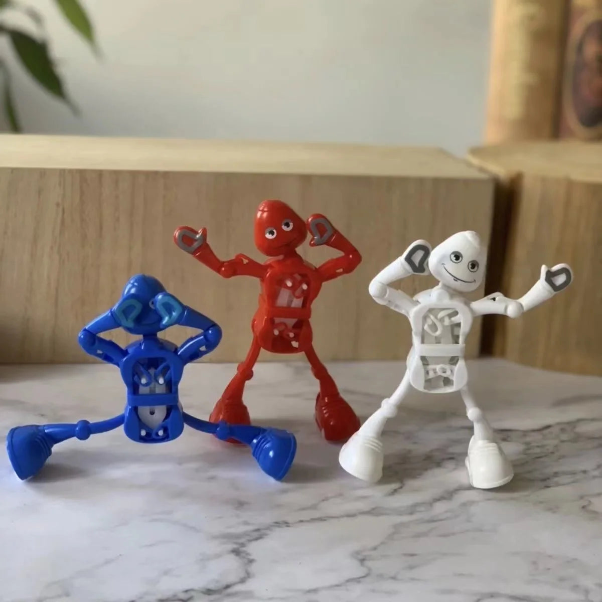 Three wind-up dancing robot toys in blue, red, and white standing on a marble surface.