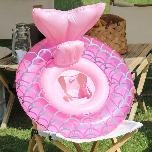 A pink inflatable swimming ring float with a scale pattern is displayed on a wooden table.