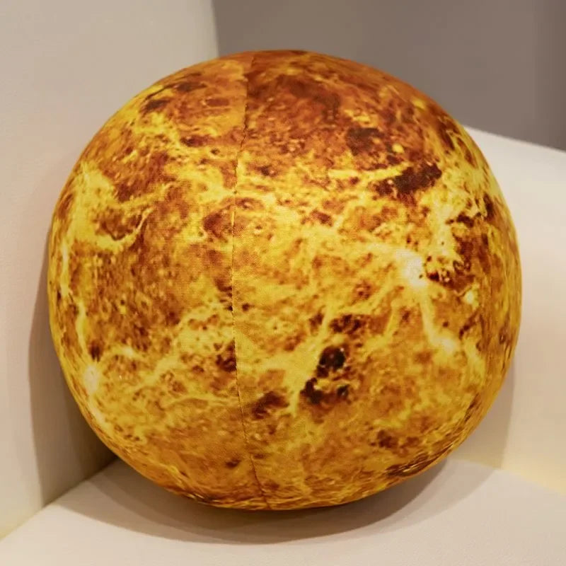 A round, golden-yellow plush toy resembling a celestial body, displayed on a white pedestal.
