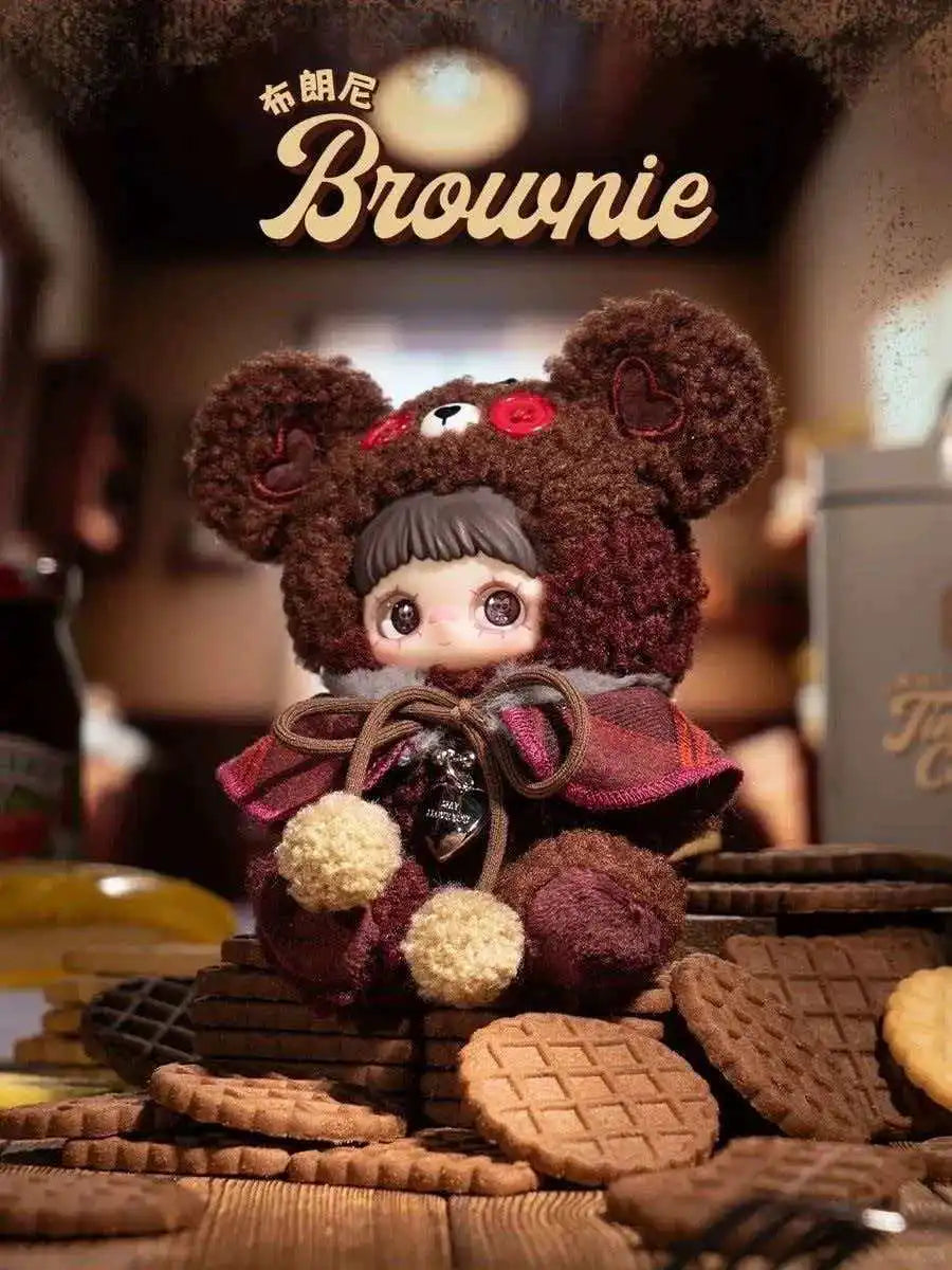 A brown bear plush charm product featuring a dark brown fur and reddish-brown clothing, displayed among cookies.