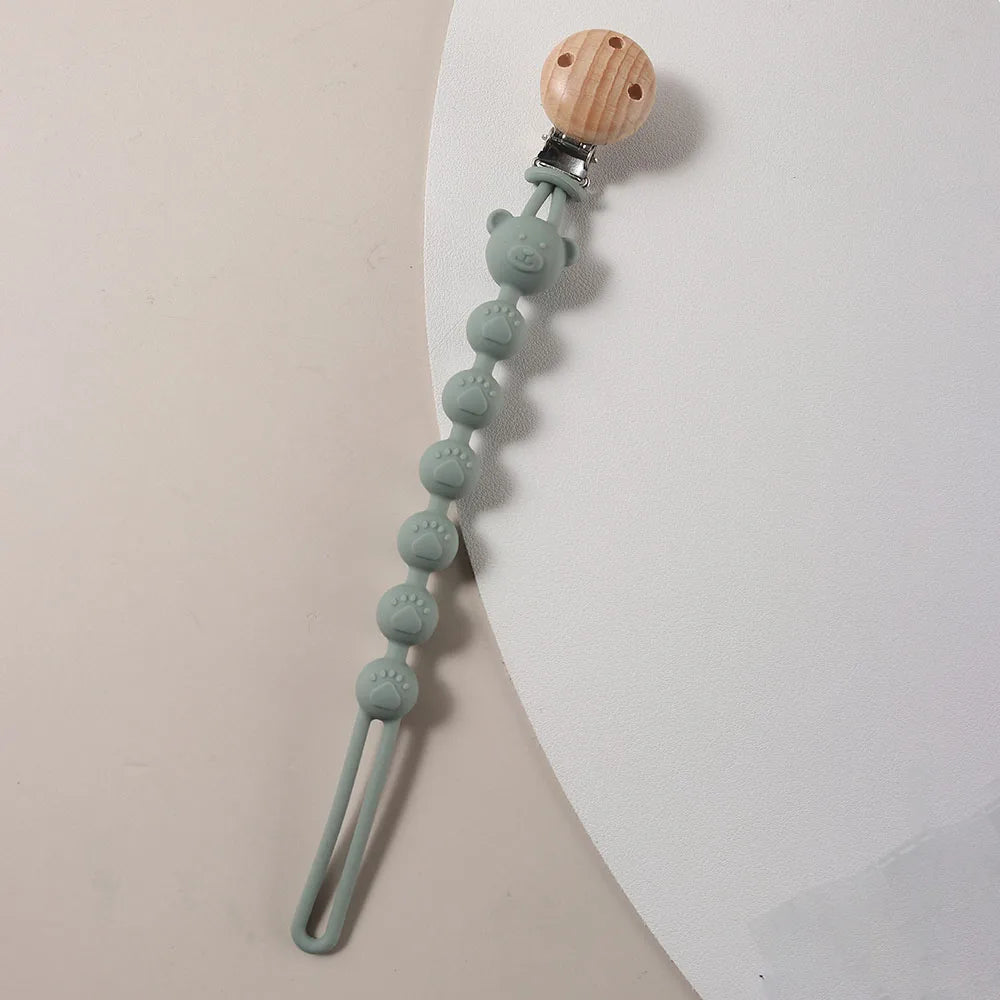 A silicone pacifier clip featuring a wooden bear paw top and a string of small, light green silicone beads.