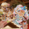 A hand holds a colorful sticker set featuring three-dimensional scenes of whimsical houses and characters.