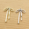 A pair of gold-toned alloy bow charms for jewelry making displayed on a neutral brown surface.