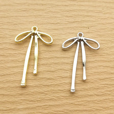 A pair of gold-toned alloy bow charms for jewelry making displayed on a neutral brown surface.