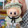 A handmade doll wearing a green plaid cape and beret set, held by a person's hand.