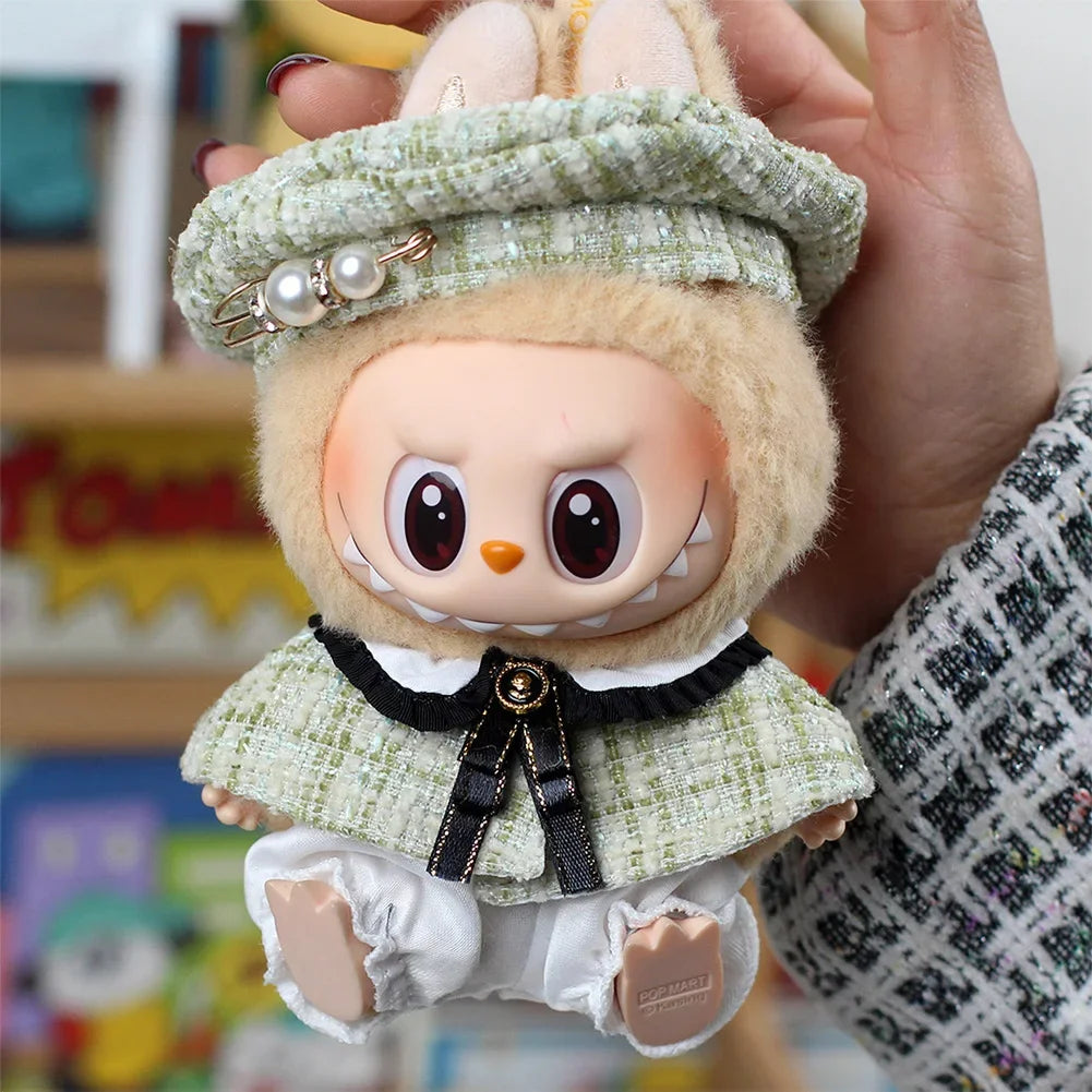 A handmade doll wearing a green plaid cape and beret set, held by a person's hand.