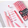 A set of six vibrant acrylic gel pens in various shades of pink and red laid out on a white grid paper.