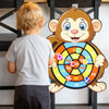 A young child is looking at a cartoon monkey dart board game with colored targets.
